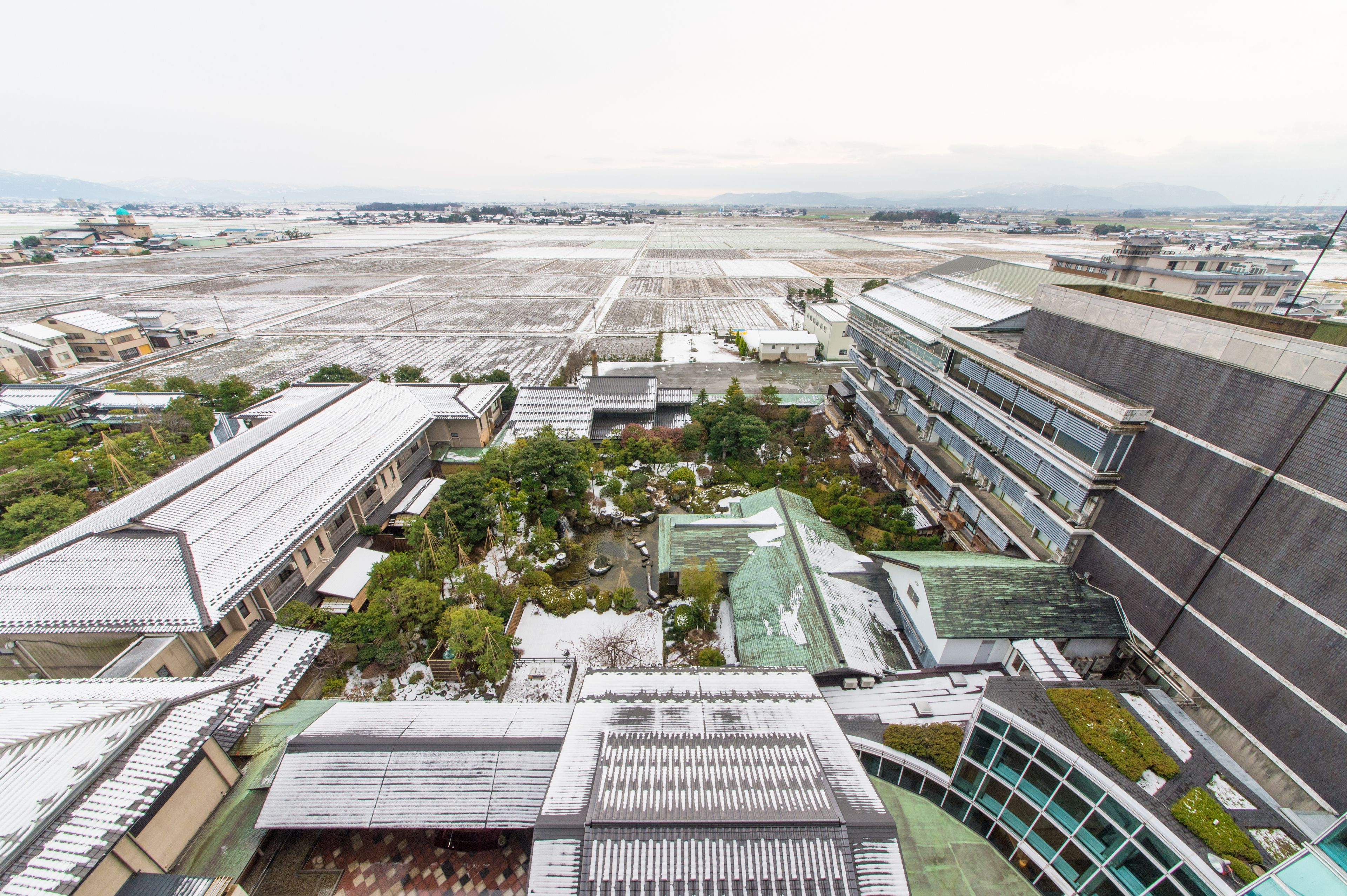 An aerial view of a large industrial area with multiple buildings, including a modern structure with a green roof and a traditional building with a tiled roof.