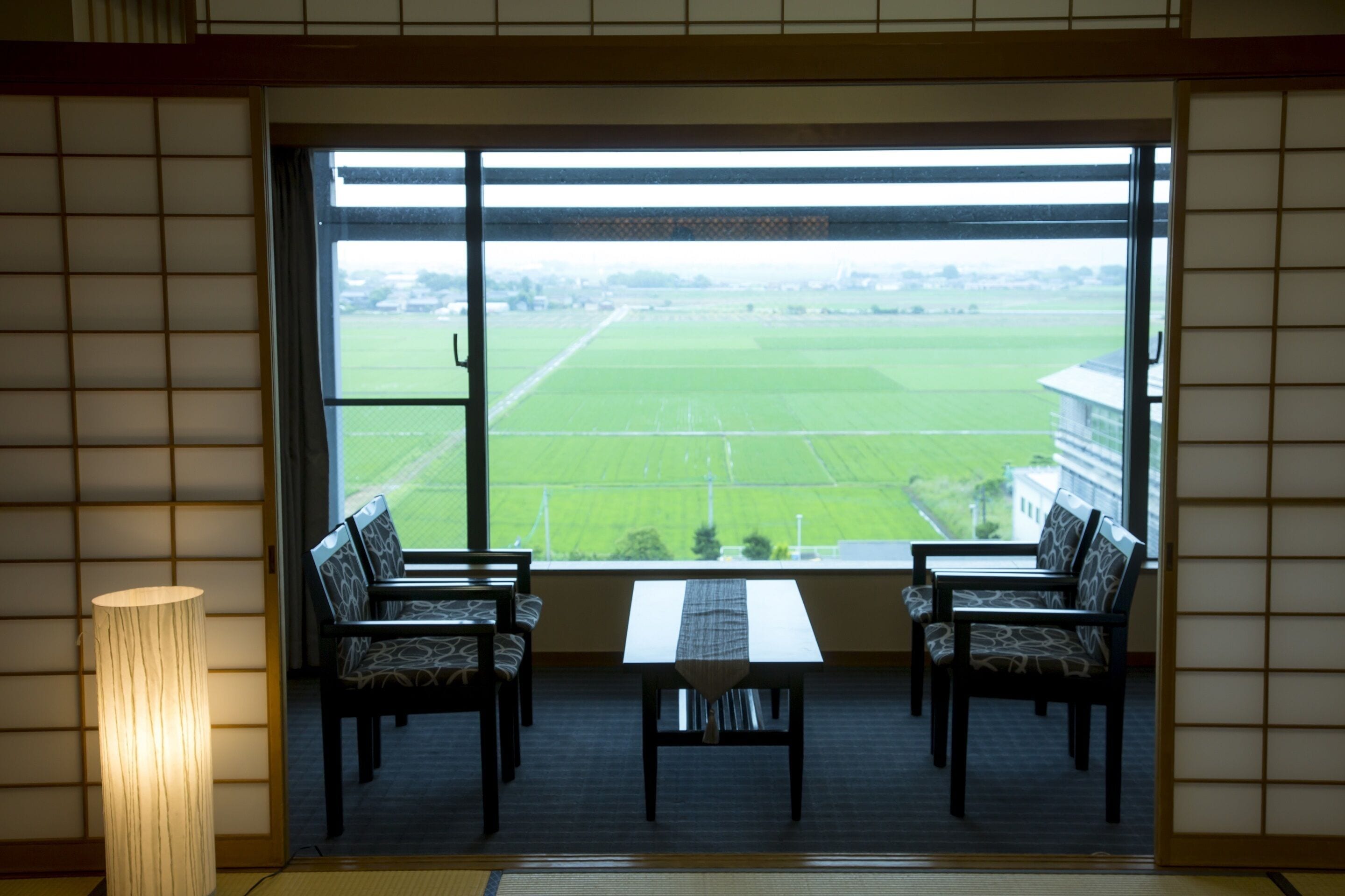 A room with a large window, two chairs, a table, and a floor lamp.