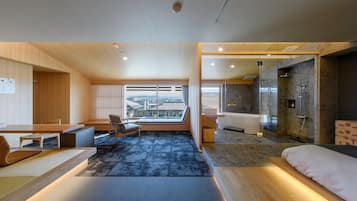 A modern hotel room with a large window, a seating area, a bathroom, and a shower area.