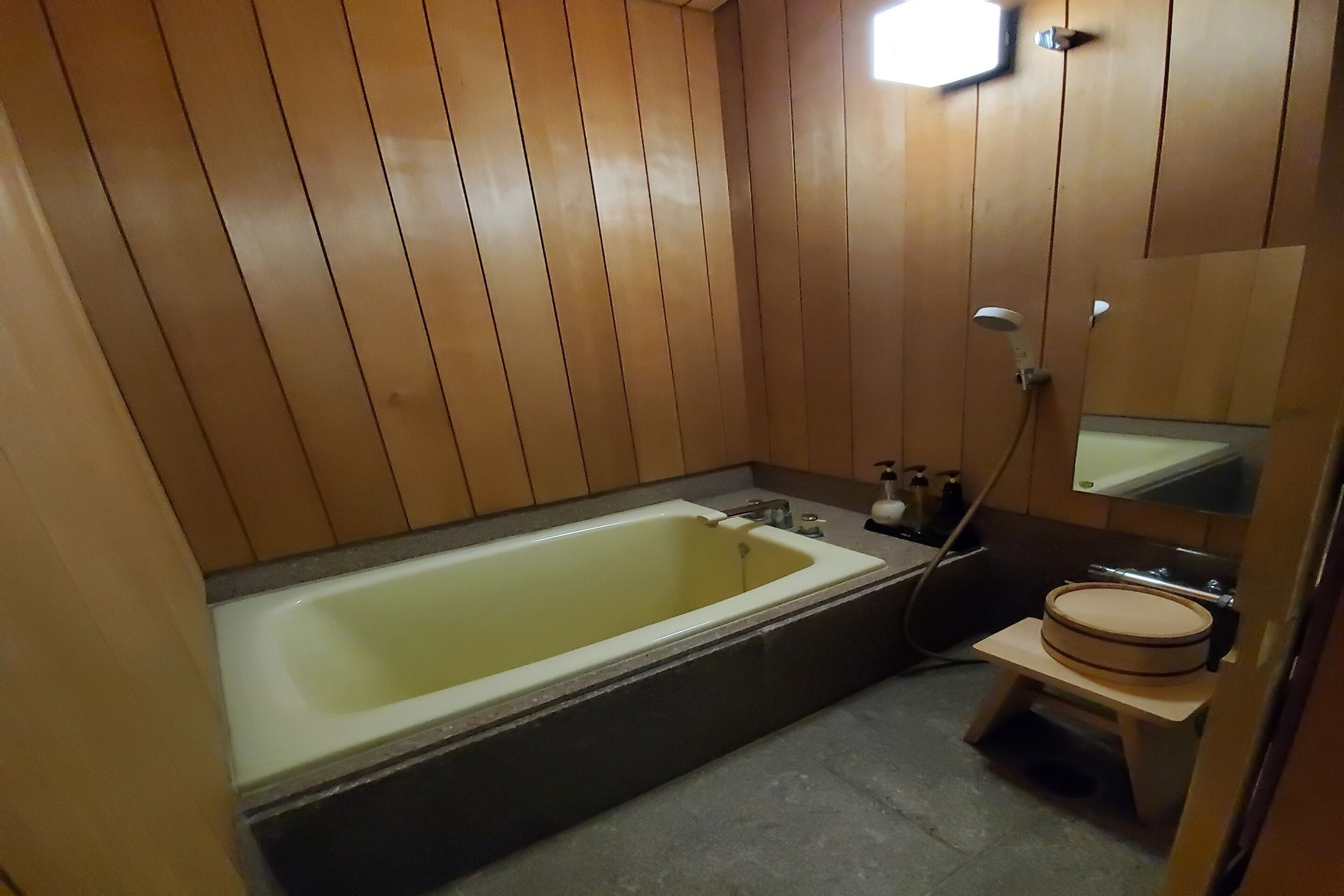 A bathroom with wooden paneling, a bathtub, a small sink with a mirror, and a toilet.