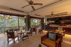 Un vaste espace de détente avec des meubles en bois, un bar et de grandes fenêtres donnant sur l’extérieur.