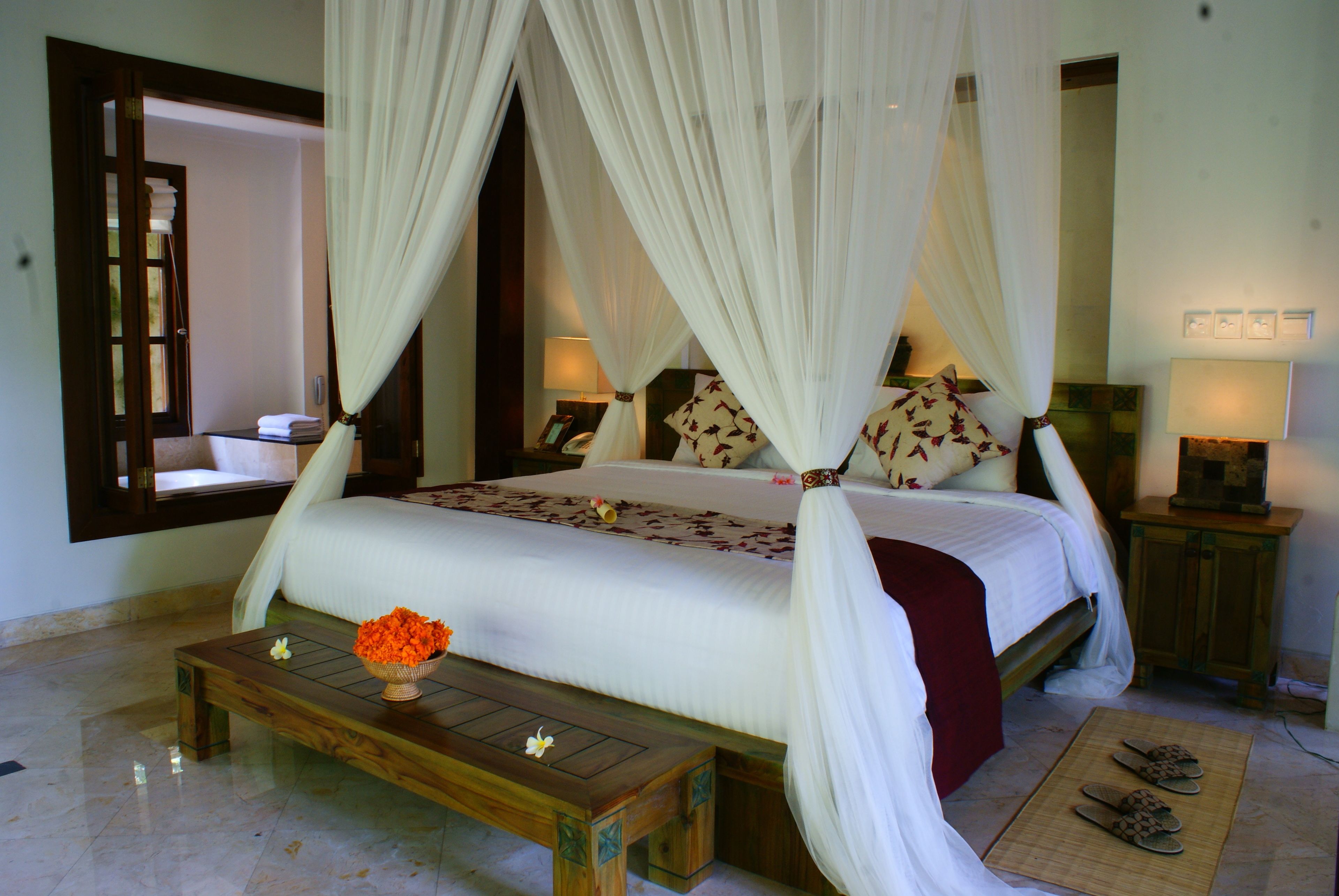 A four-poster bed with a canopy, a bedside table with a vase of flowers, and a wooden bench.