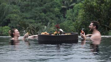 Dos personas en un jacuzzi con una plataforma flotante que contiene flores y alimentos.