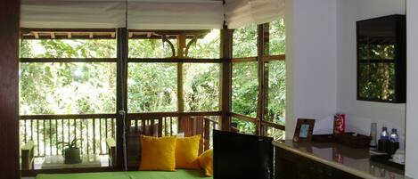 Una habitación con un sofá verde, televisión y ventana con vistas a zonas verdes.