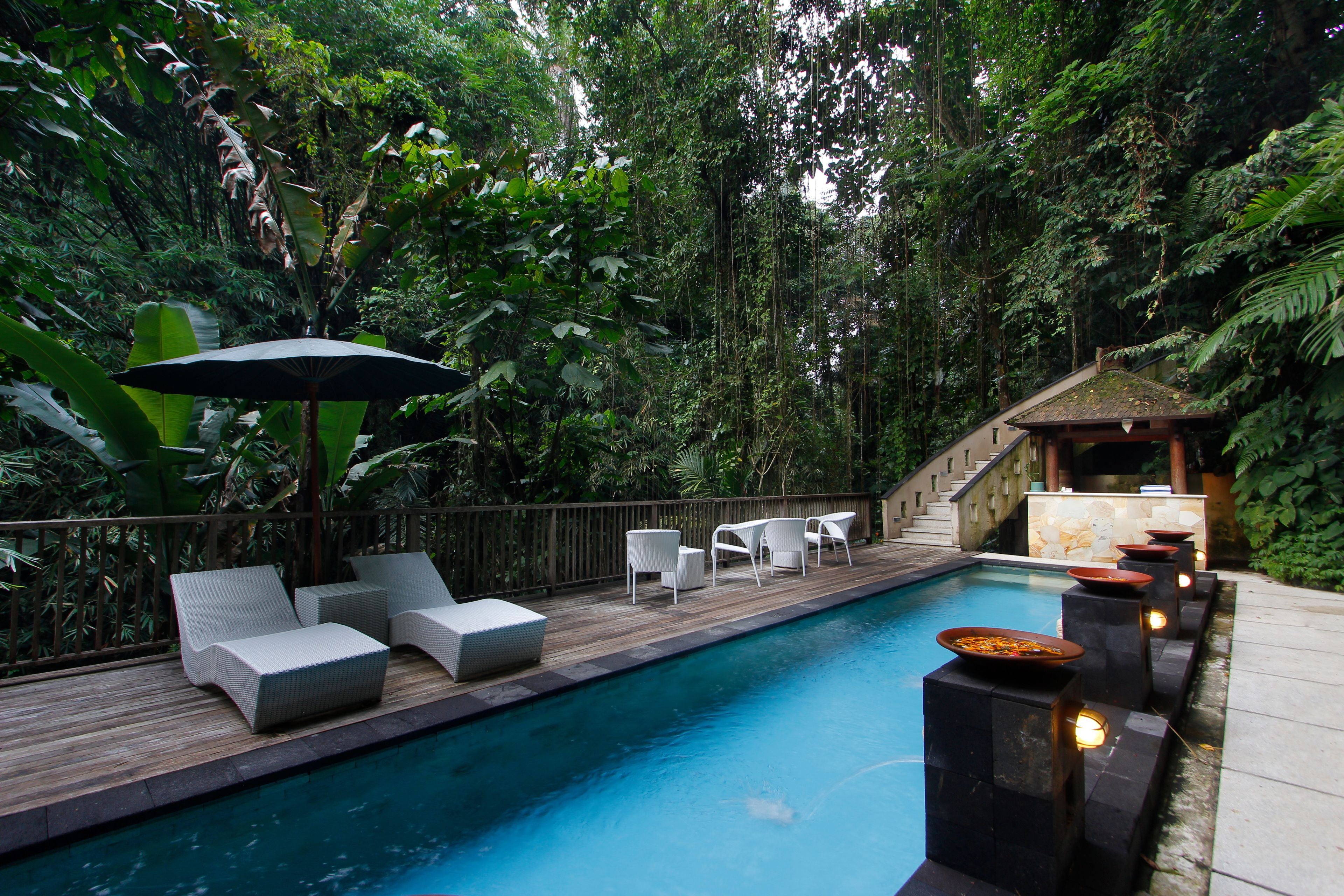 Un espace aménagé au bord de la piscine, avec des chaises longues, une table et un bar de style polynésien.