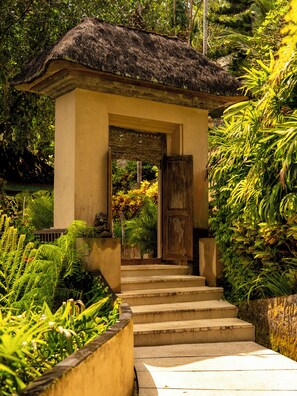 Une petite construction dotée d’un toit de chaume, d’une porte en bois et d’un escalier en béton menant à l’entrée.