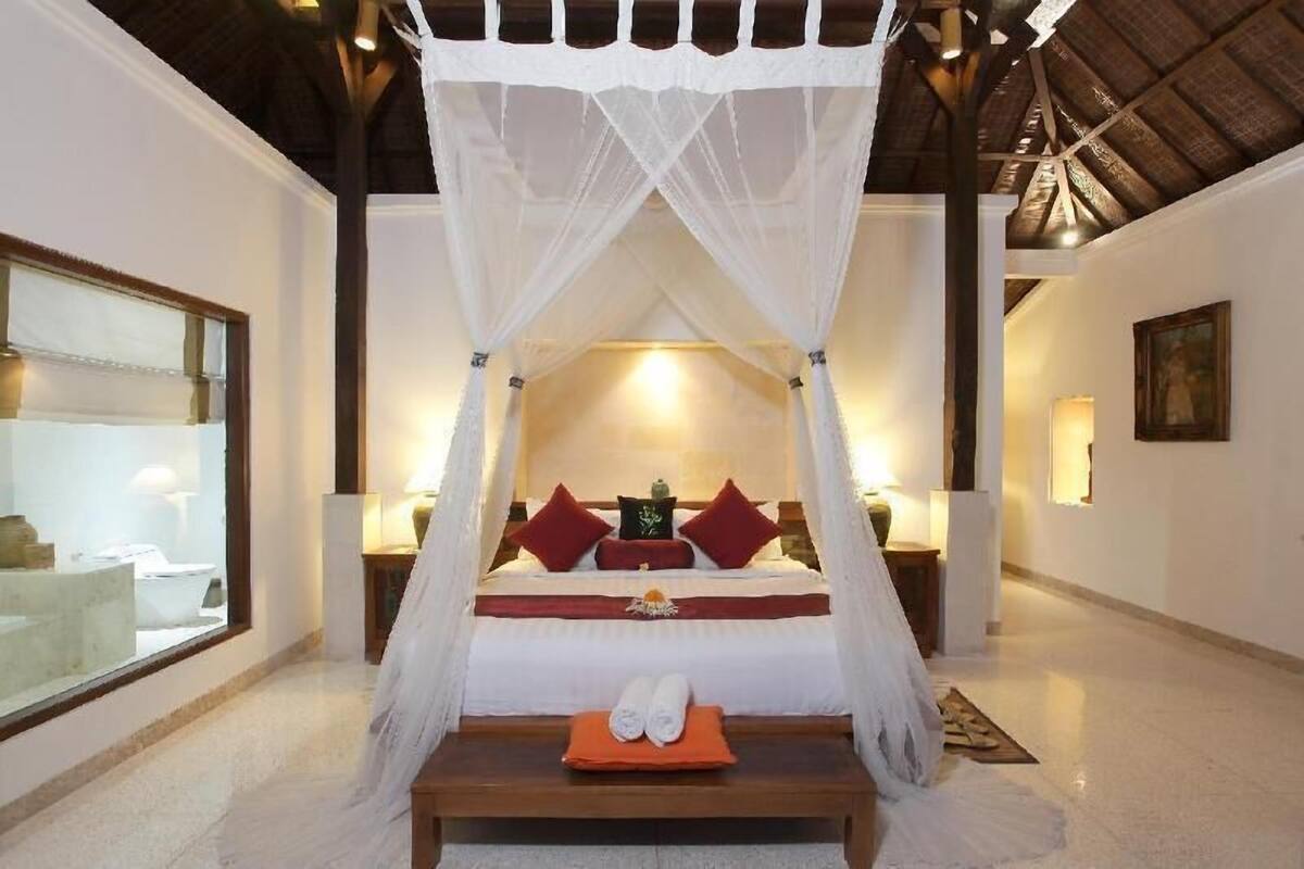 Un dormitorio con cama a dosel, una mesita de noche con lámpara y una ventana con vistas.