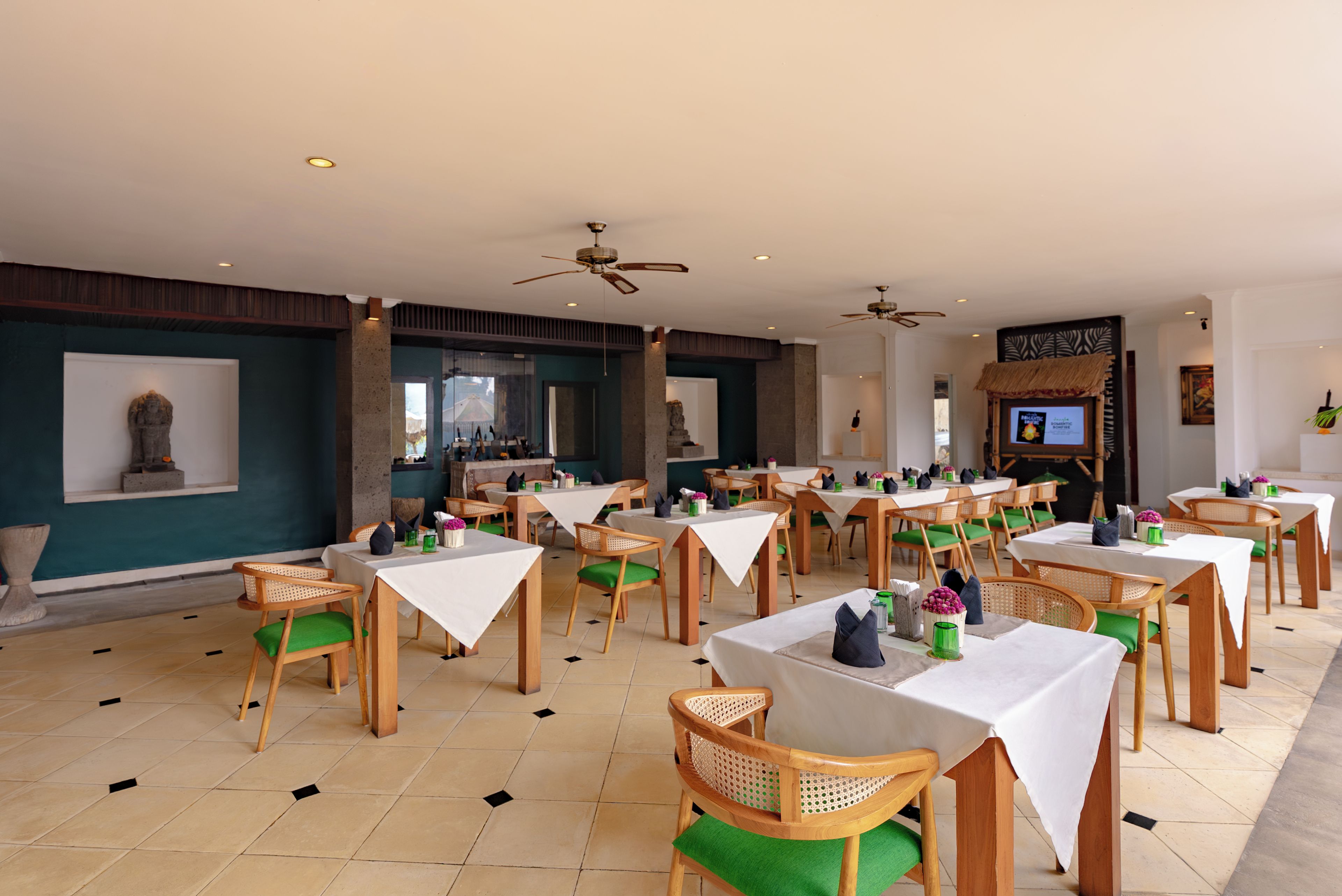 Un vaste espace dédié à la salle à manger, avec de nombreuses tables et chaises, des ventilateurs de plafond et des œuvres d’art accrochées aux murs.