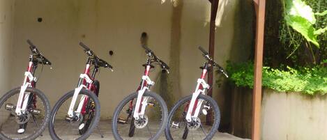 Four bicycles parked under a wooden structure with a concrete wall in the background.