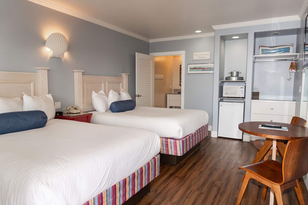 A hotel room with two beds, a dining table, a microwave, and a small kitchen area.