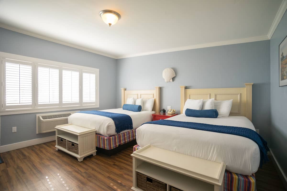 A bedroom with two beds, a window with blinds, a heater, and a wall-mounted light fixture.