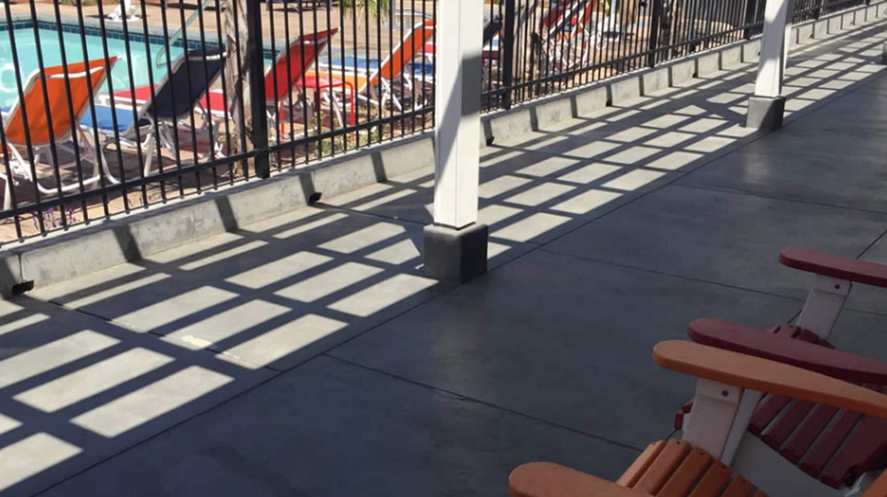 A poolside area with a tiled walkway, a fence, and a row of beach chairs.