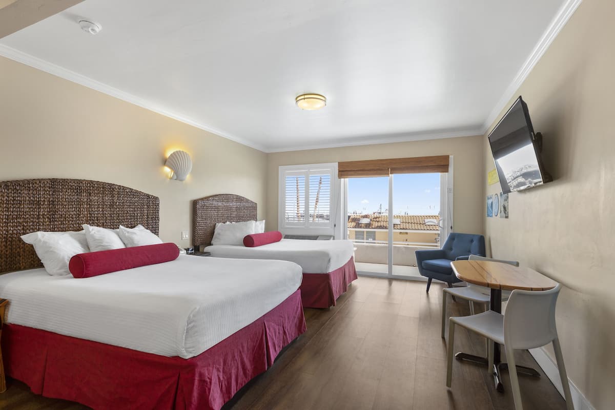 A hotel room with two beds, a desk, and a chair.