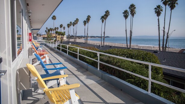 A balcony with rows of beach chairs, a railing, and a view of the beach and ocean.