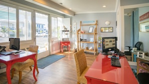 A modern office space with a red desk, wicker chairs, a computer, and a bookshelf.