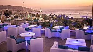 A rooftop lounge with white furniture and a view of the city and ocean at sunset. - DoubleTree by Hilton Hotel Aqaba (Aqaba)