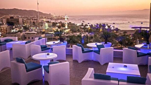 Terraza en la azotea con mobiliario blanco y vistas a la ciudad y al océano al atardecer.