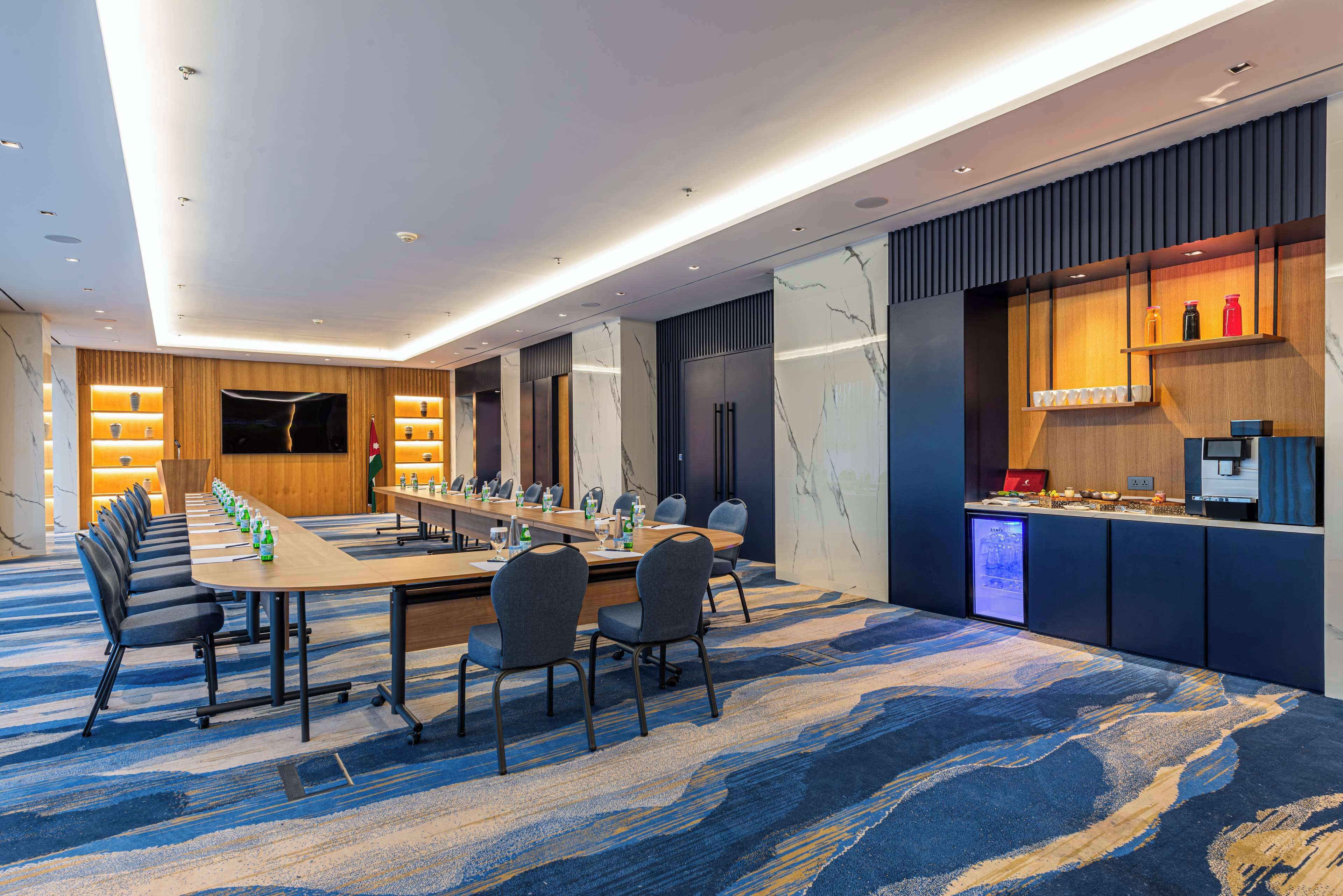 A modern conference room with a long table, chairs, and a TV screen.