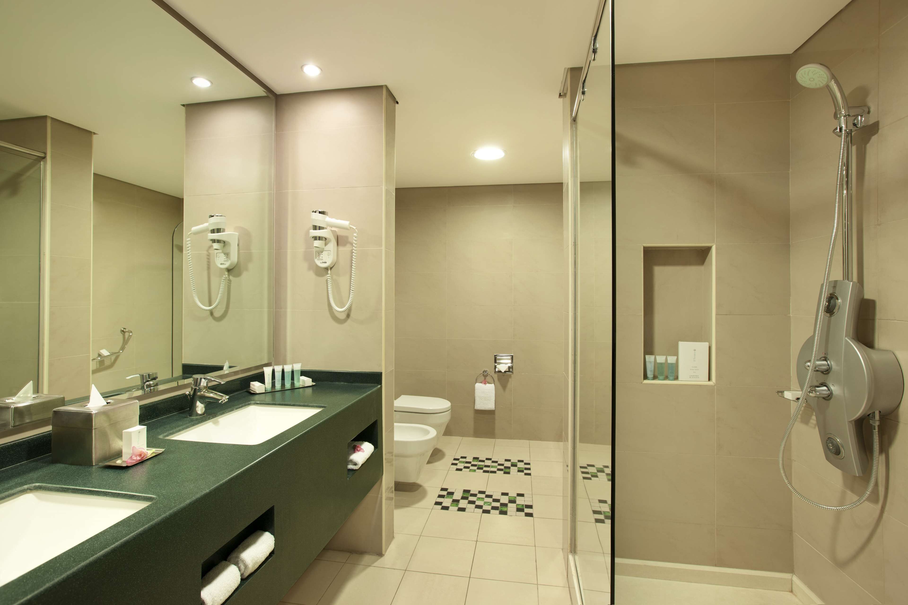 A modern bathroom with two sinks, a glass shower enclosure, and a toilet.