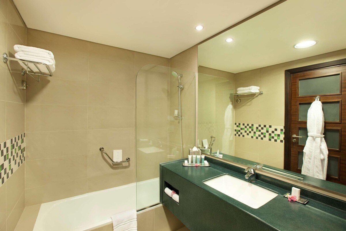 A modern bathroom with a glass-enclosed shower, a bathtub, and a sink with a green countertop.