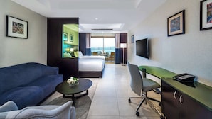 Habitación de hotel con cama, sofá, escritorio, televisor y cuadros en las paredes.
