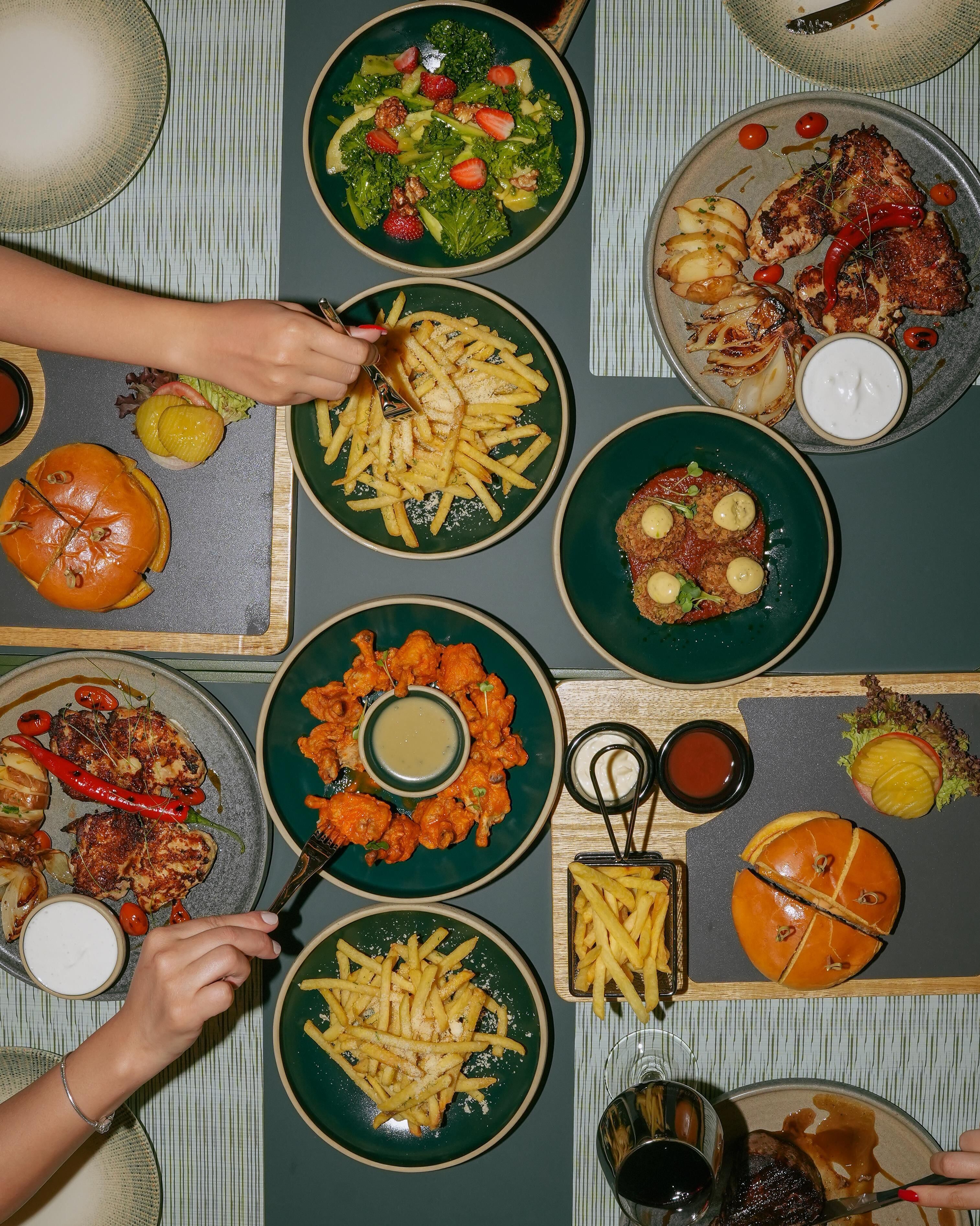 A table set with various dishes including burgers, fries, and salads, suggesting a casual dining environment.