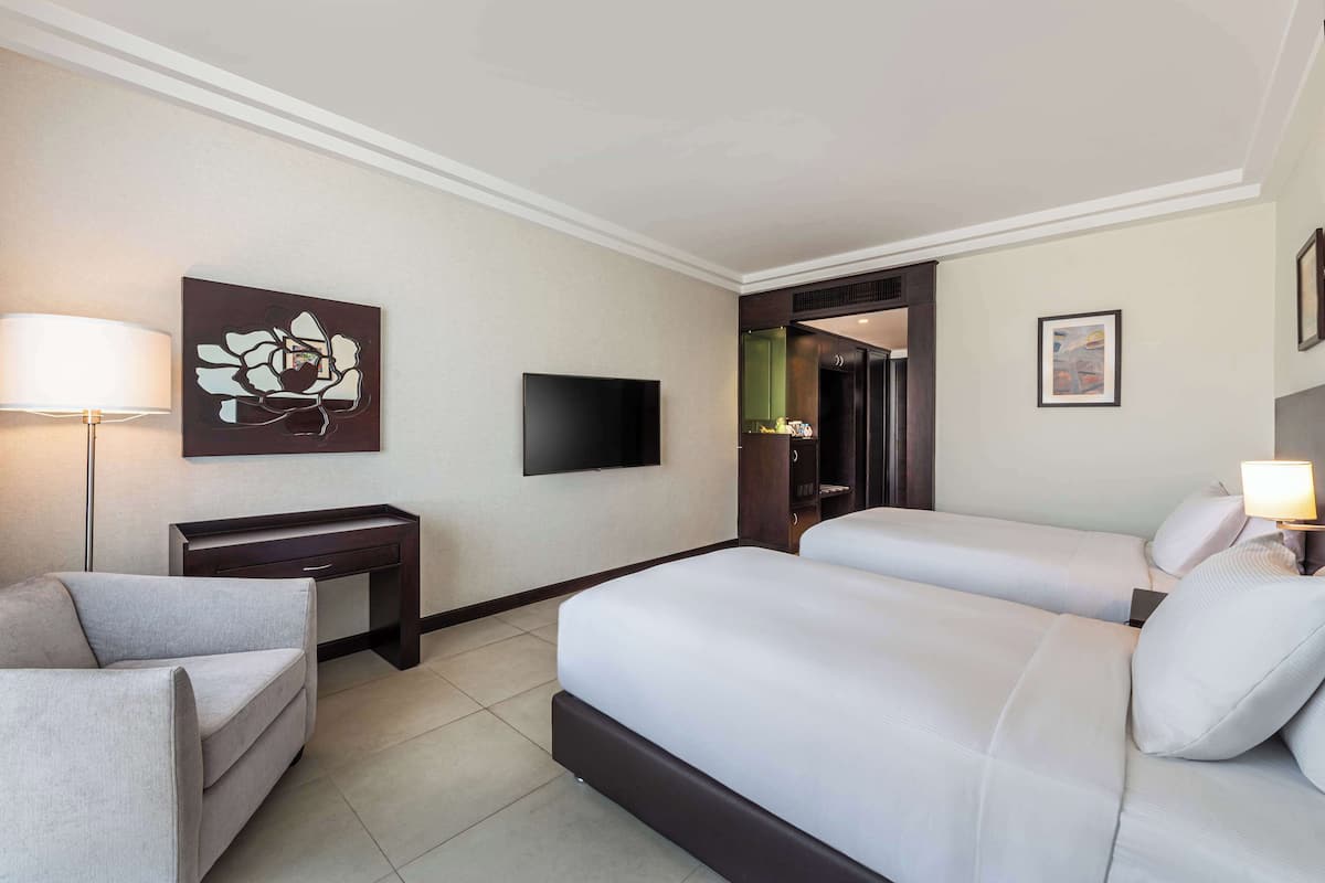 A hotel room with a large bed, a desk, a chair, a TV, and a painting on the wall.