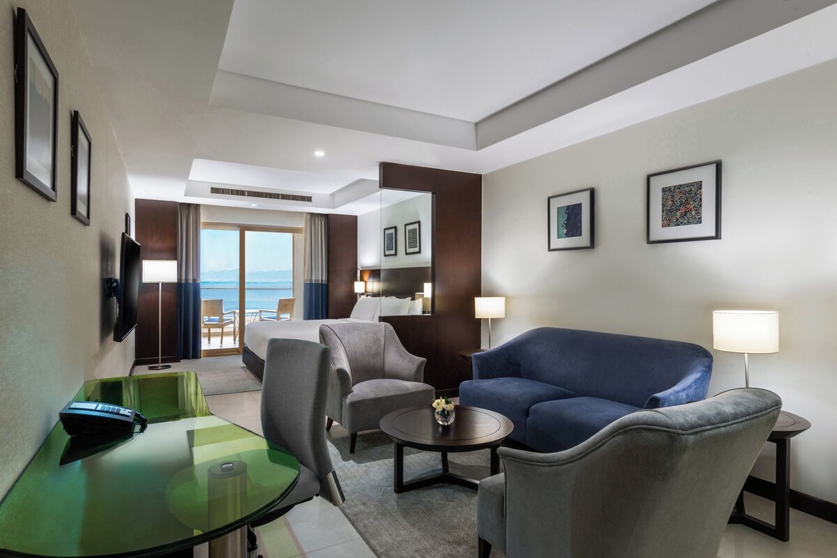 Una habitación de hotel con una cama, dos sillones, un sofá, una mesita de vidrio y un televisor.