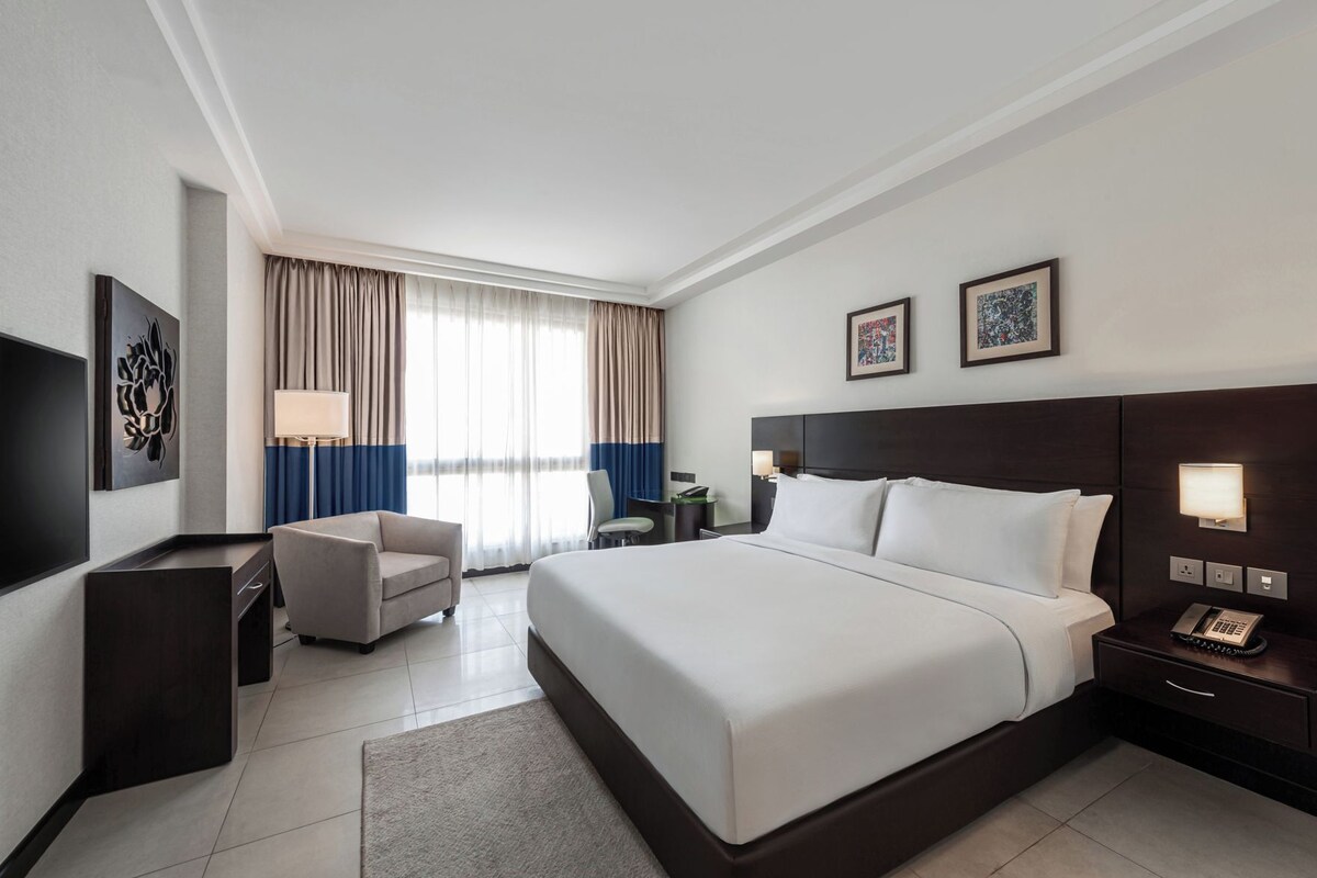 Una habitación de hotel con una cama grande, un escritorio, una silla, un televisor y una ventana con cortinas.