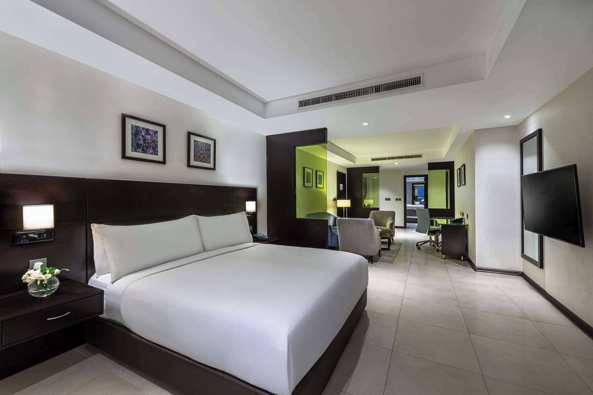 A modern hotel room with a large bed, bedside tables, a flat-screen TV, and a desk area with chairs.