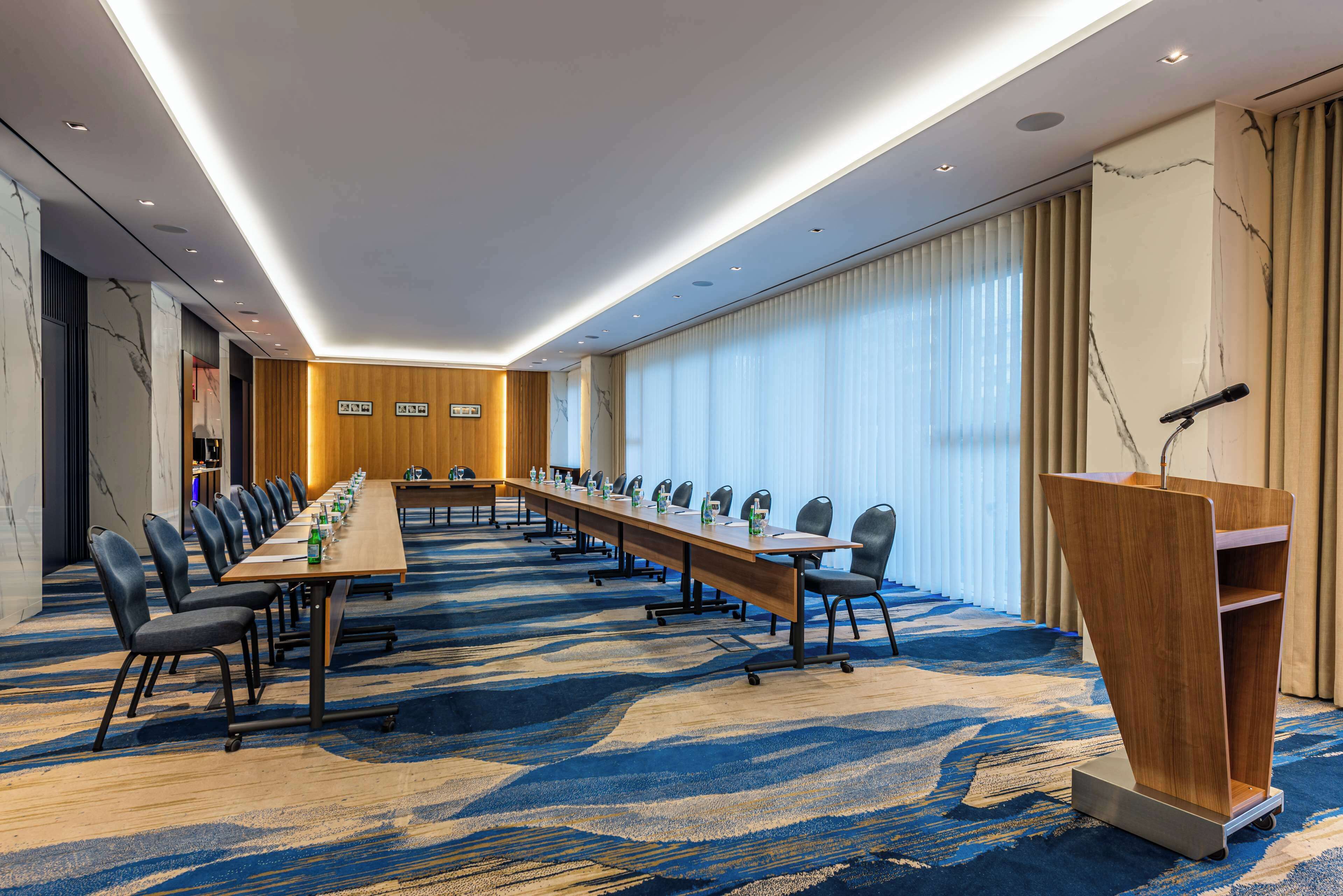 A conference room with a long table, chairs, a podium, and a large window with curtains.