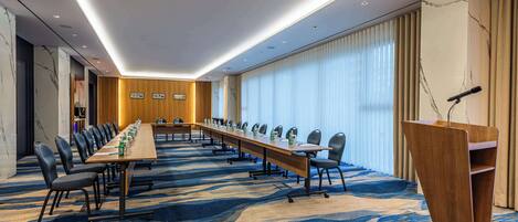A conference room with a long table, chairs, a podium, and a large window with curtains.