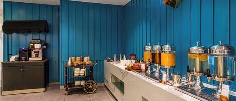 Una barra de desayuno con una máquina de café, un carrito de pan y diversas bebidas.
