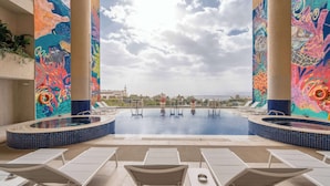 Un área de piscina en la azotea con murales coloridos, sillones de descanso y vistas al horizonte de la ciudad.