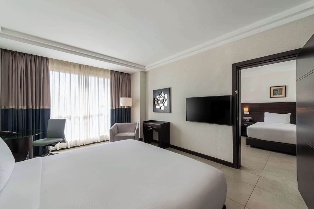 A hotel room with a large bed, a desk with a lamp, a chair, a TV, and a wardrobe.