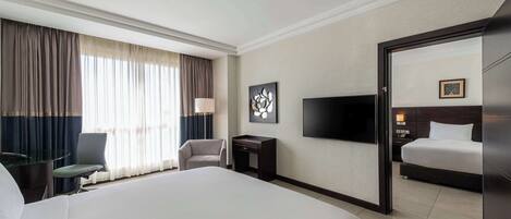 A hotel room with a large bed, a desk with a lamp, a chair, a TV, and a wardrobe.