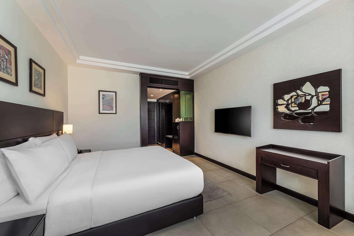 A hotel room with a large bed, a bedside table, a flat-screen TV, and artwork on the walls.