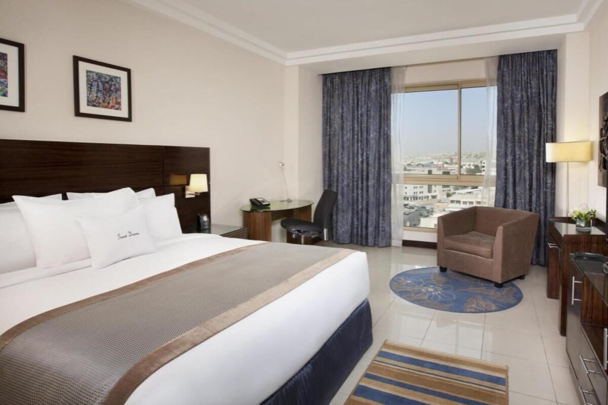A hotel room with a large bed, a desk, a chair, and a view of the city.