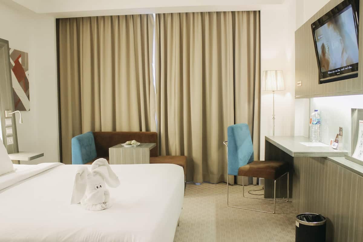 A hotel room with a bed, a desk, two chairs, a TV, a trash bin, and a curtain.