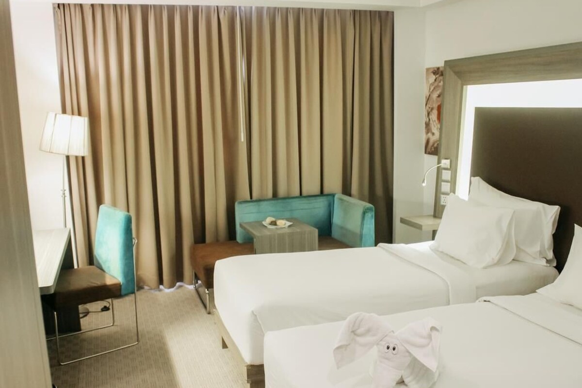 A hotel room with two beds, a desk, a chair, a small table, and a window with curtains.