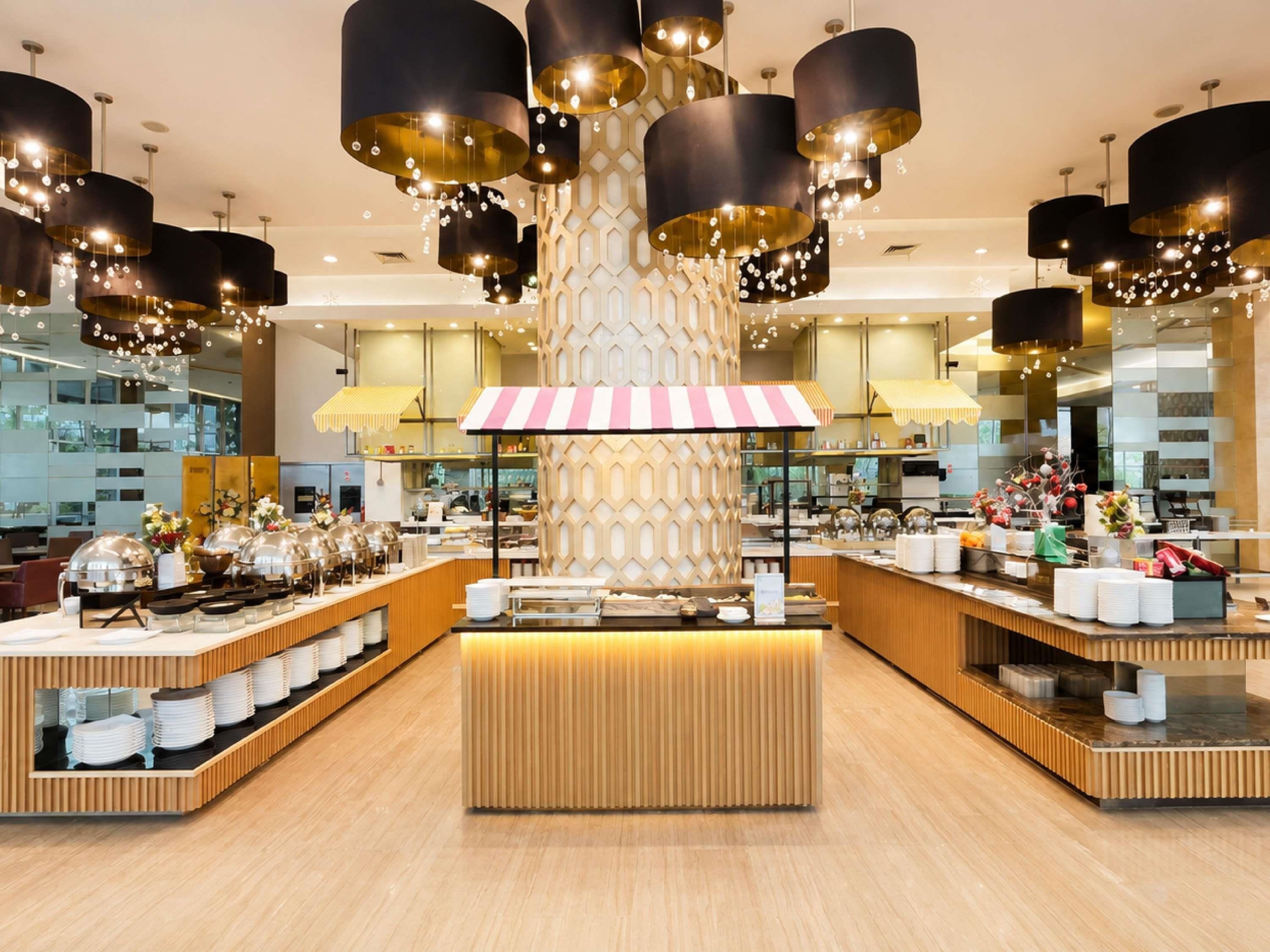 Un moderno vestíbulo de hotel con una recepción central, varias estaciones de comida y luminarias contemporáneas.