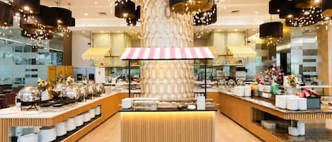 A modern hotel lobby with a central reception desk, multiple food service stations, and contemporary lighting fixtures.
