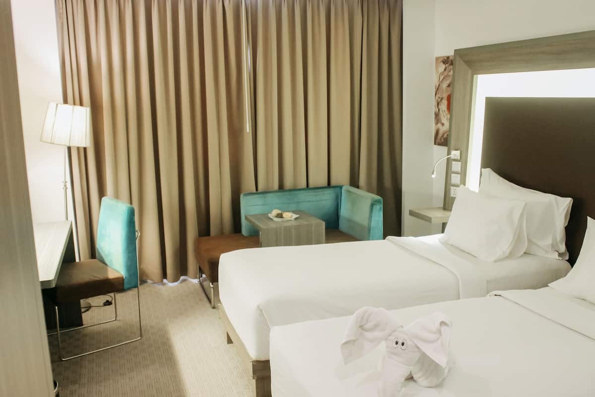 A hotel room with two beds, a desk, a chair, a small table, and a large window with curtains.