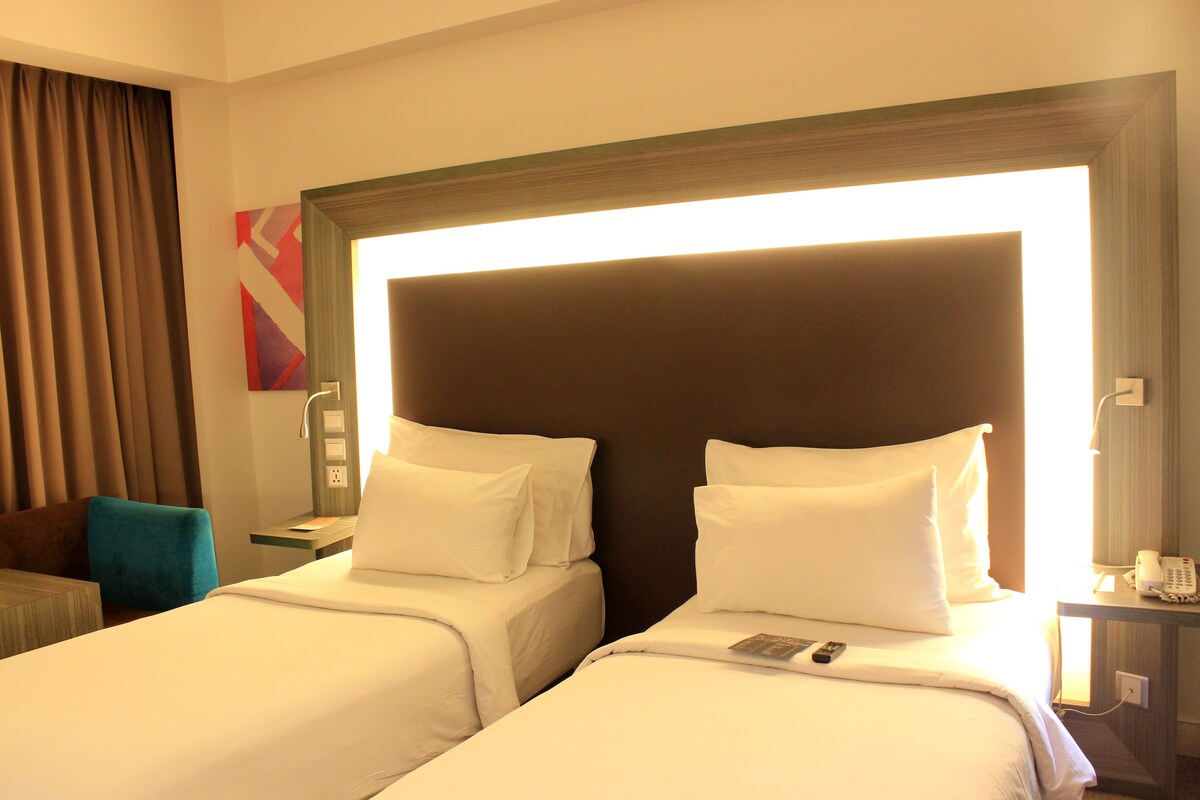 A hotel room with two beds, a desk, a chair, and a nightstand with a phone.