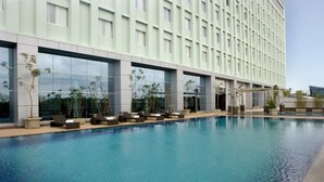 A modern hotel with a swimming pool, lounge chairs, and a large building facade. - Novotel Bangka Hotel & Convention Centre (Pangkalpinang)