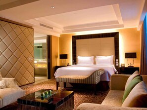 A hotel room with a large bed, a sofa, a coffee table, and a wall with a textured design.
