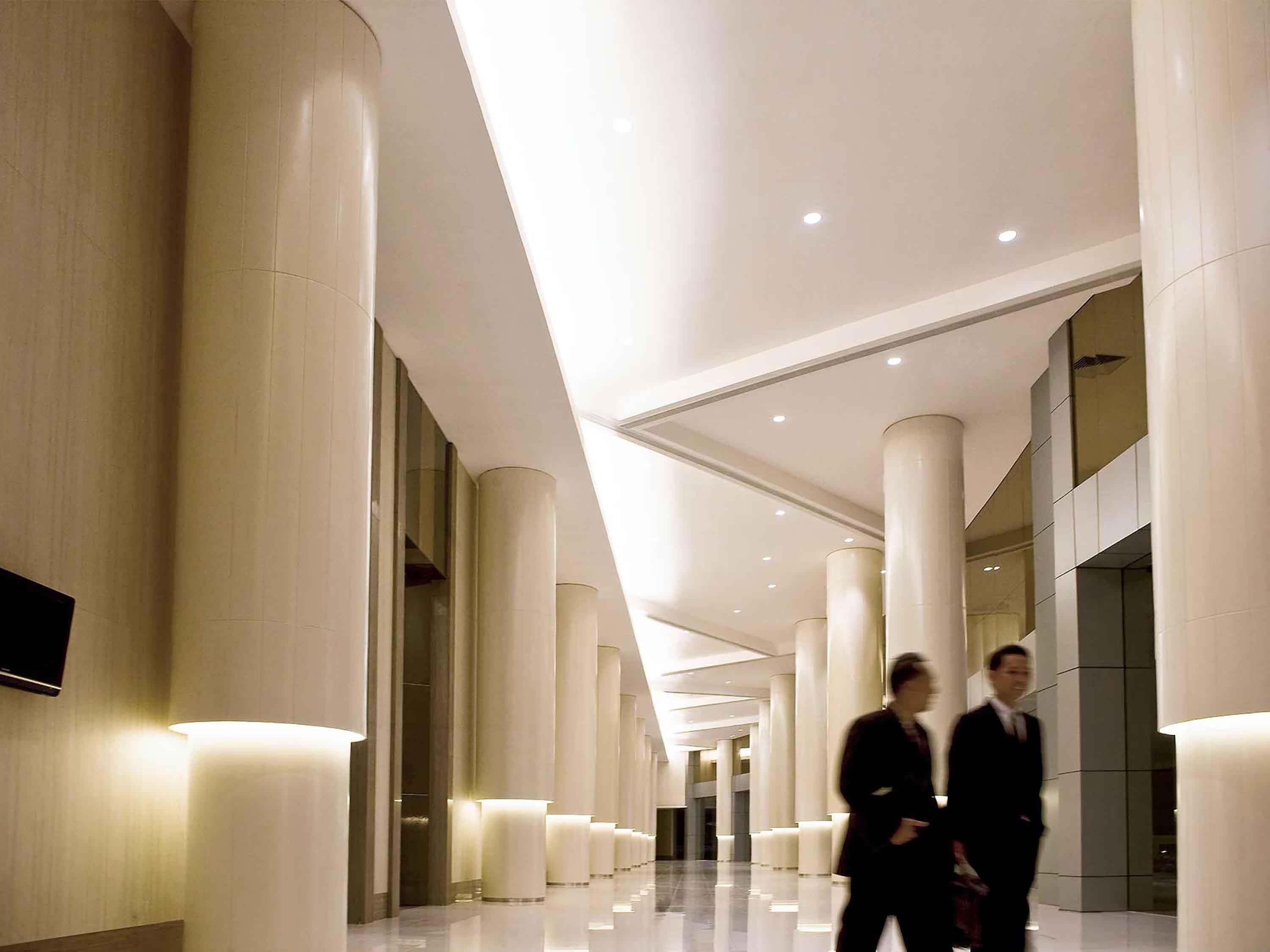 Un pasillo con columnas grandes, techo plano e iluminación empotrada.