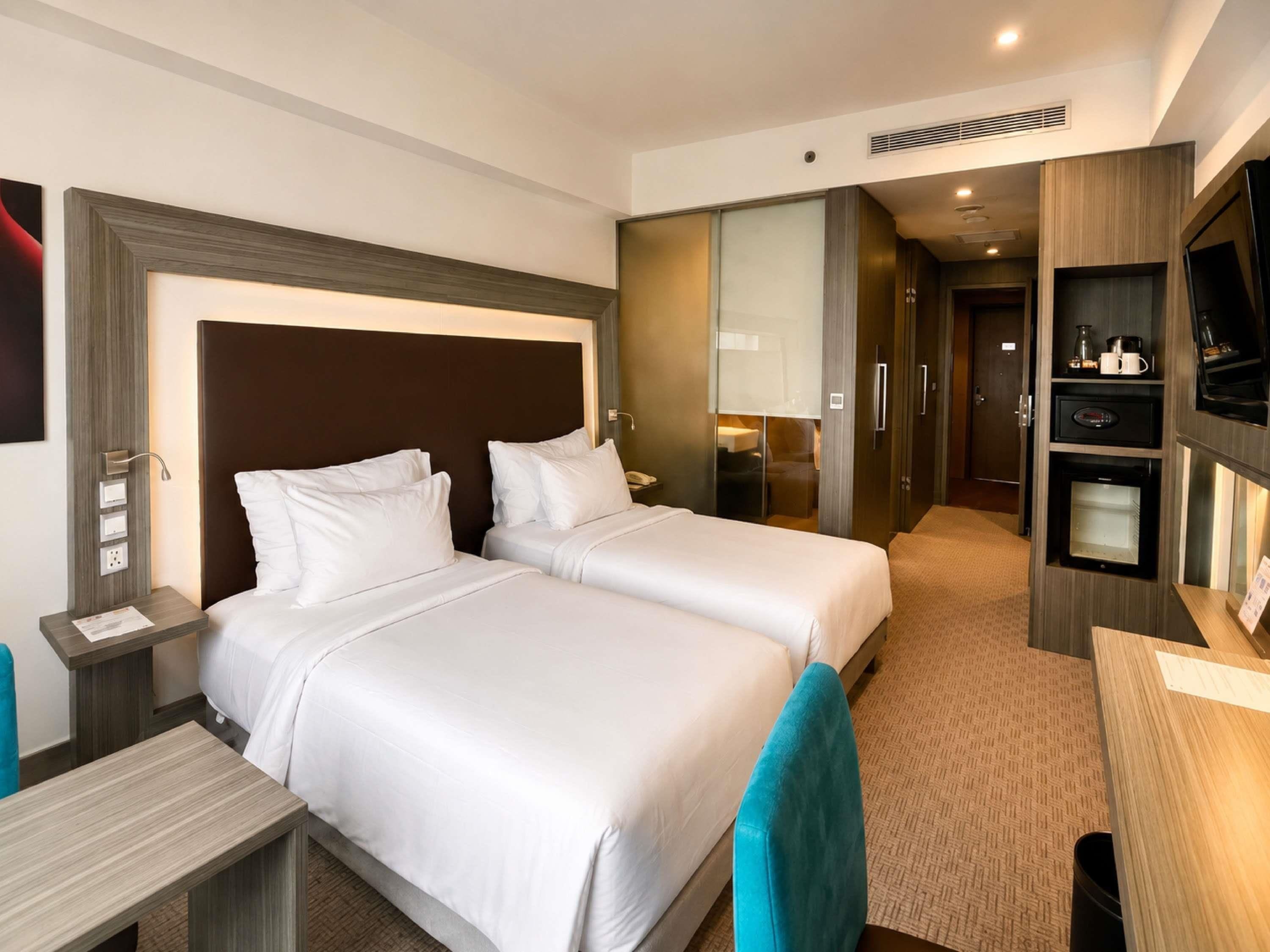 Ein Hotelzimmer mit zwei Betten, einem Schreibtisch, einem Fernseher und einer Minibar.