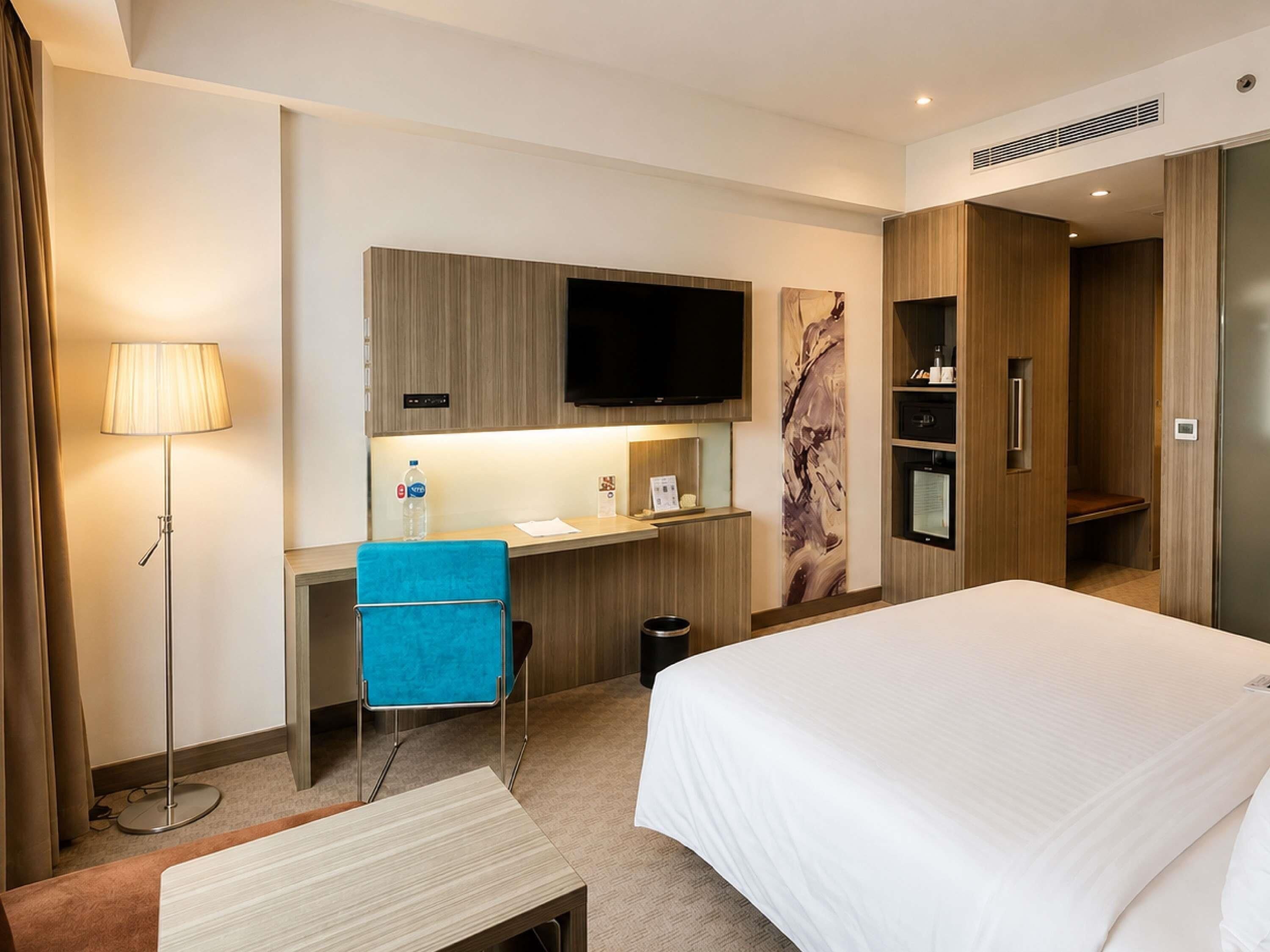 Une chambre d’hôtel équipée d’un lit, d’un bureau, d’une chaise, d’une télévision et d’un mini-bar.