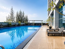 A rooftop pool with clear blue water, surrounded by lounge chairs and potted plants.